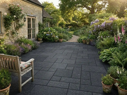 Black granite paving patio in a lush garden setting with flowers and a wooden bench.